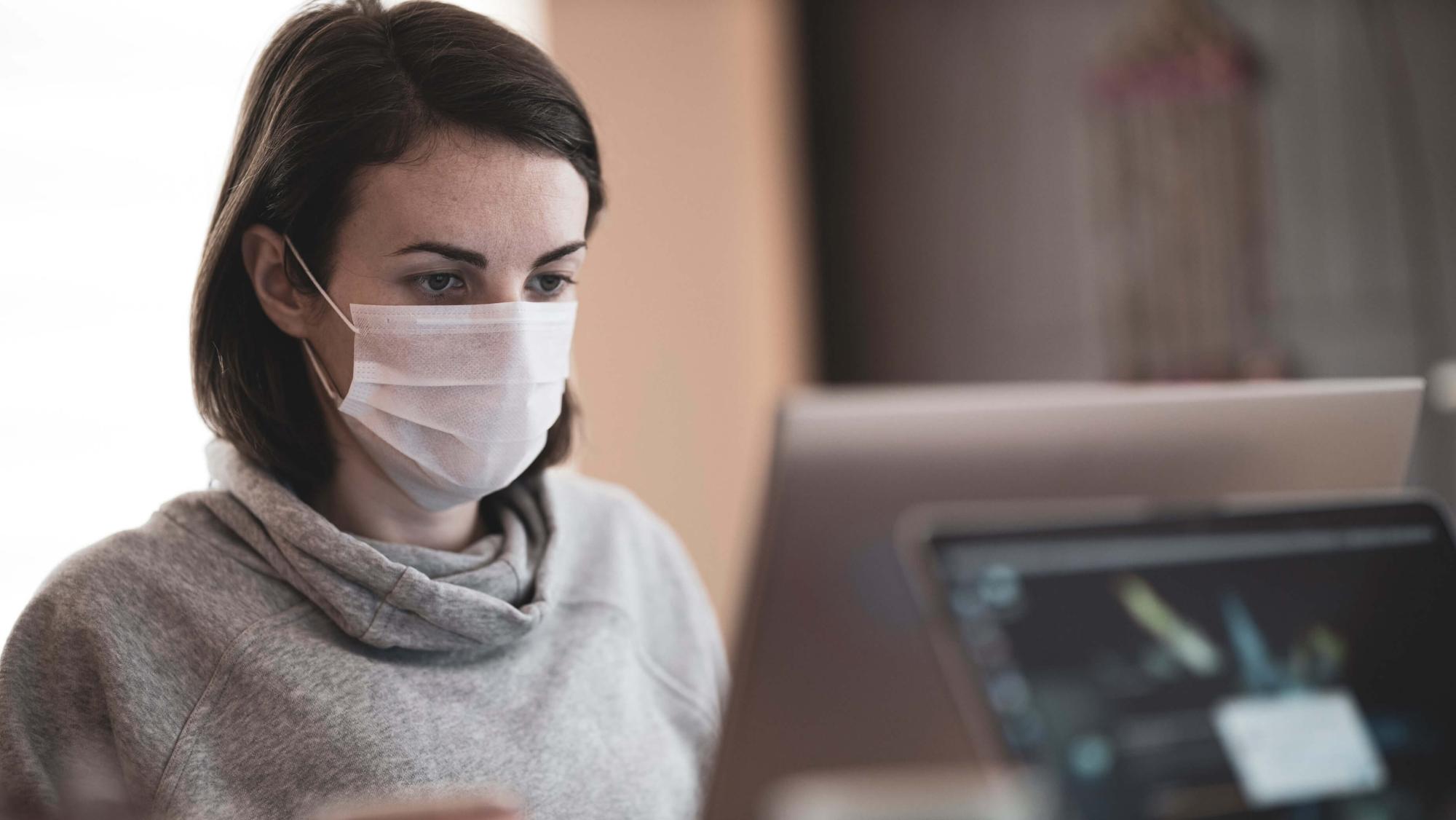 Woman wearing mask using computer
