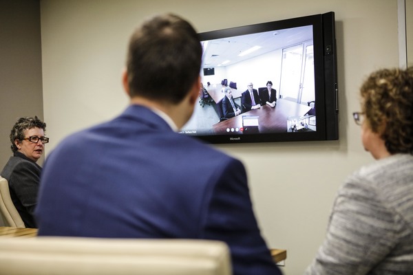 A group of mediators of the Supreme Court in a mediation room , communicate with another group of people using video conferencing.