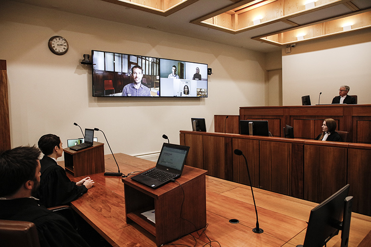 An upgraded courtroom in use with judge, associate and barristers showing upgraded all the available new digital technology such as video conferencing on a digital screen.